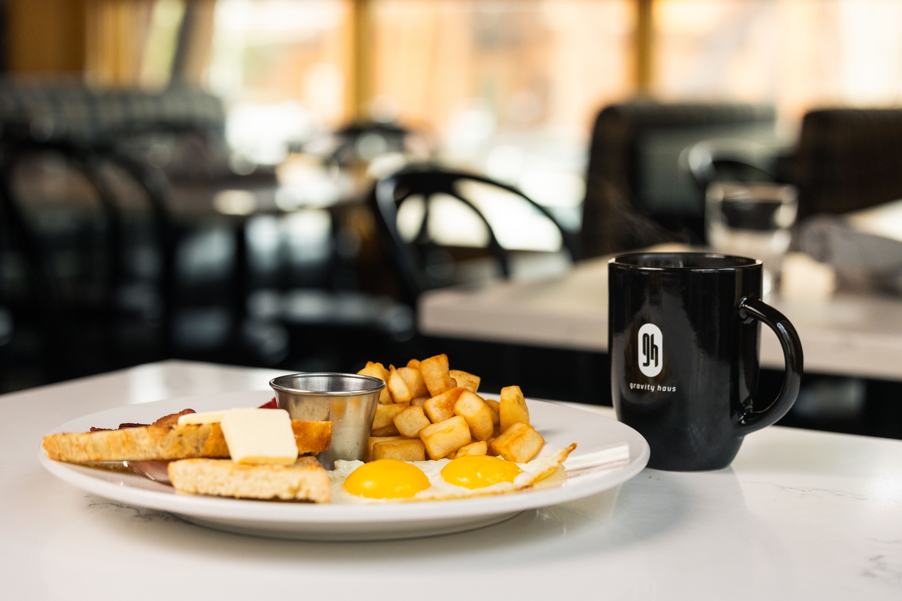 Une assiette de petit-déjeuner avec des toasts, des œufs et des pommes de terre rissolées, posée sur une table blanche.