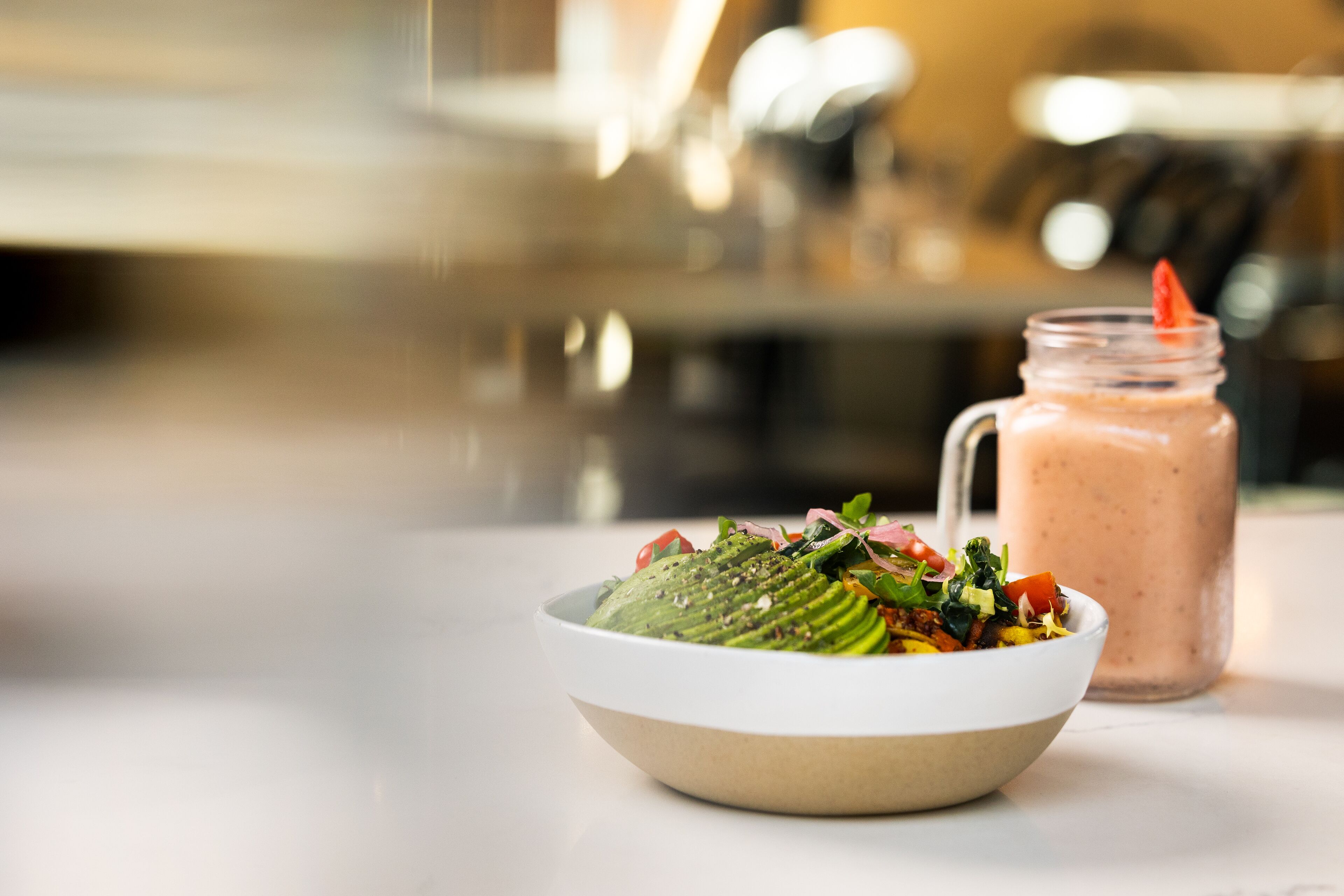 A bowl of salad with a smoothie in a glass jar.