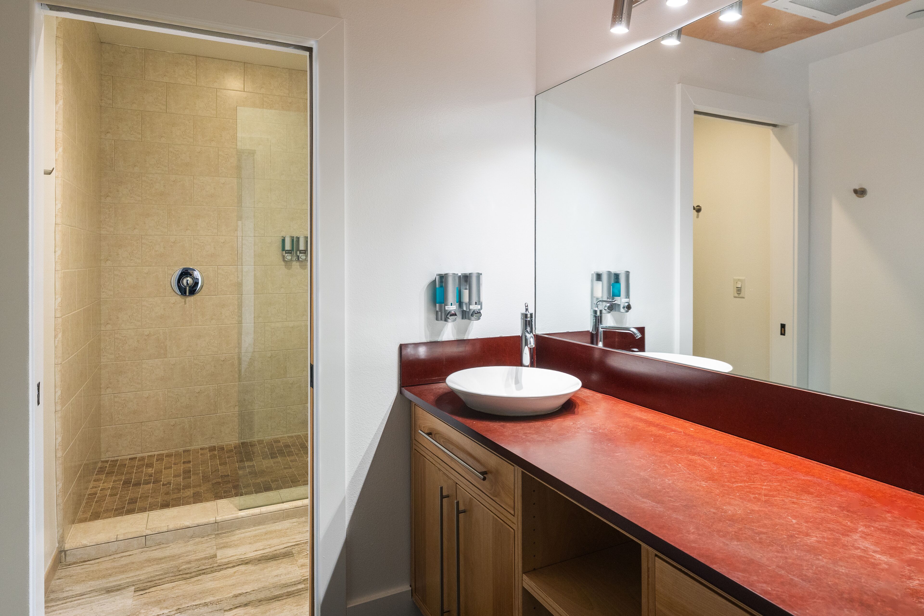 Un baño moderno con cabina de ducha de vidrio, un espejo grande y encimera roja.