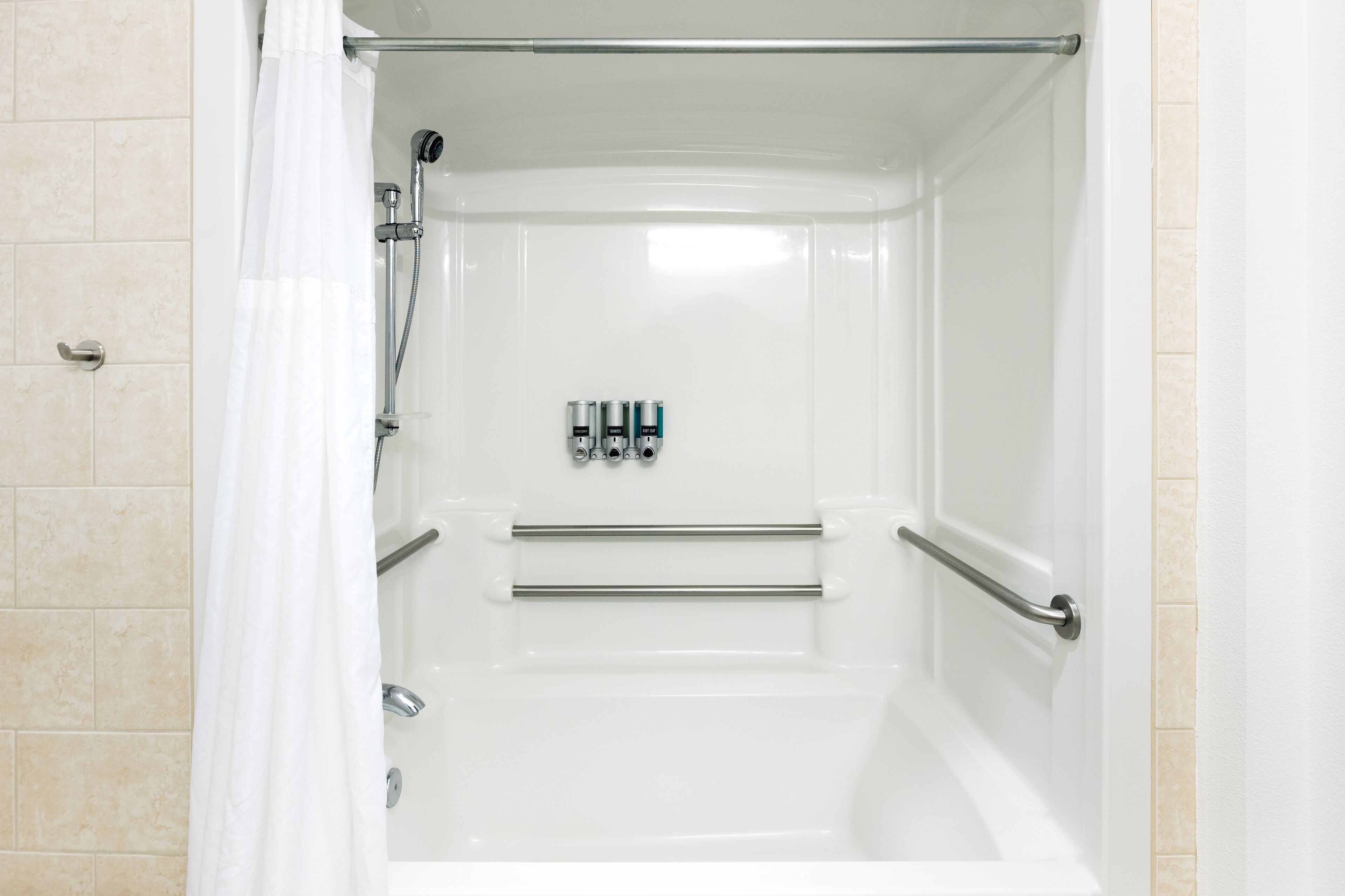 A white shower enclosure with a glass door, a showerhead, and a handrail.