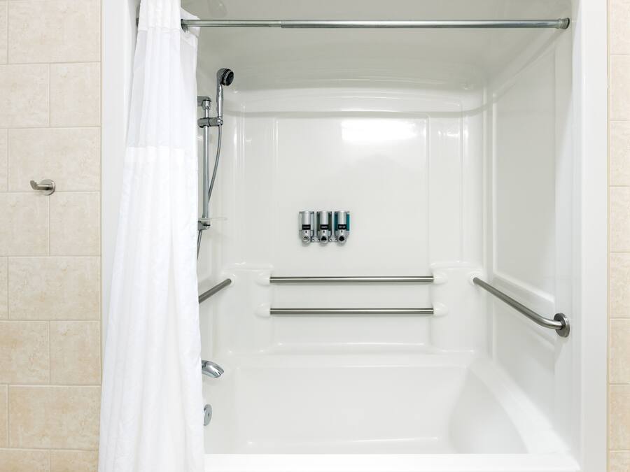 A white shower enclosure with a glass door, a showerhead, and a handrail.