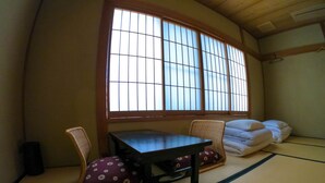 A tatami room with a low table, two chairs, and a large window with wooden frames. - Miyagawacho Hanakanzashi- Hostel (Kyoto)