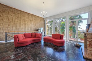 A spacious room with a brick wall, large windows, a red sofa, and a chandelier.