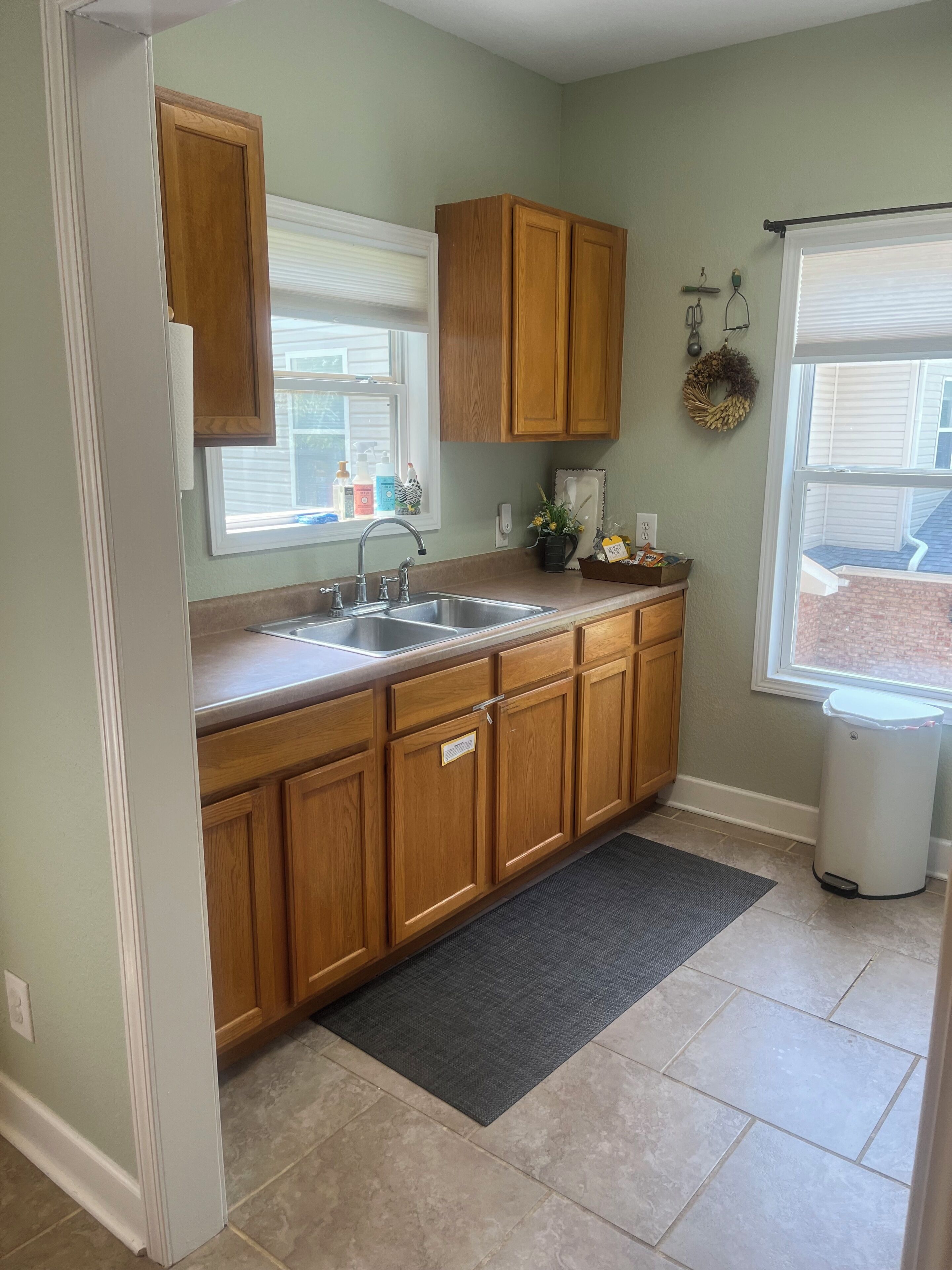 A kitchen with wooden cabinets, a double sink, and a window with blinds.