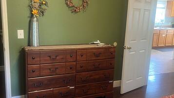 A room with a wooden dresser, a door, a patterned bedspread, and a wall with a wreath.