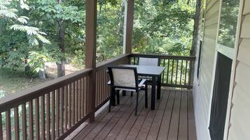 A covered porch with a table and chairs, surrounded by wooden railings and a view of greenery.