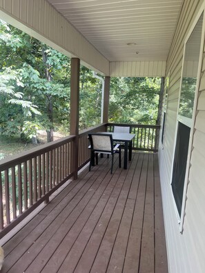 Une véranda avec une table et des chaises, entourée de balustrades en bois et offrant une vue sur la verdure.