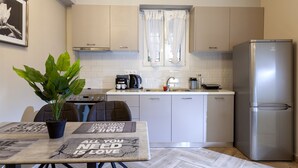 Une cuisine moderne avec des meubles blancs, un réfrigérateur en acier inoxydable, une table à manger agrémentée d’une plante en pot et une fenêtre ornée de rideaux légers.