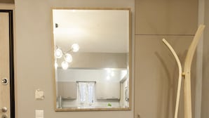 Une pièce dotée d’un parquet en bois disposé en motif «point de Hongrie», d’un fauteuil en cuir marron, d’un grand lampadaire blanc et d’un miroir accroché au mur.