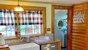 A kitchen with a window, a sink, a dishwasher, and a sign that reads "Cabin Sweet Cabin".