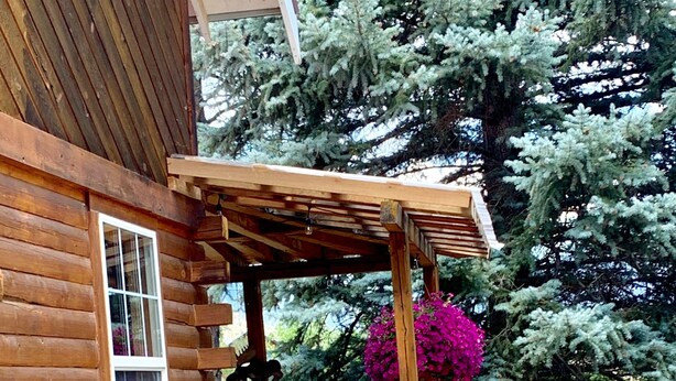 A wooden cabin with a porch, a welcome sign, a rocking chair, and a bear statue.