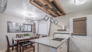 Een moderne keuken met een centraal eiland, een eethoek met een houten tafel en stoelen, en een grote spiegel boven het aanrecht.