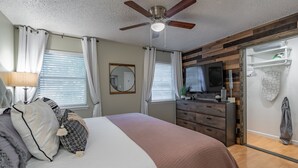 Een slaapkamer met een bed, een plafondventilator, een dressoir en een inloopkast.