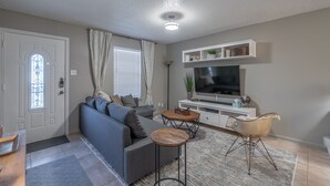 Een woonkamer met een grijze bank, een televisie, een wit tv-meubel en een kleine ronde salontafel.