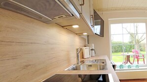 A modern kitchen with a wooden backsplash, stainless steel appliances, and a large window offering a view of the outdoors. - Studio Apartment Arnis - Apartments Landhaus Siemens in Kappeln (Kappeln)