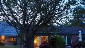 A brick house with a tiled roof, a large tree in front, and outdoor seating. - Studio Apartment Arnis - Apartments Landhaus Siemens in Kappeln (Kappeln)