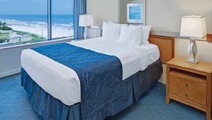 A hotel room with a large bed, a nightstand, a lamp, and a view of the beach. - Two Bedroom Luxury Condo, Daytona Beach (1732048) (Daytona Beach)