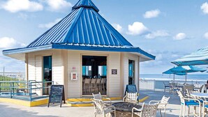 A beachside gazebo with a blue roof and beige walls, surrounded by beach chairs and umbrellas. - Two Bedroom Luxury Condo, Daytona Beach (1732048) (Daytona Beach)