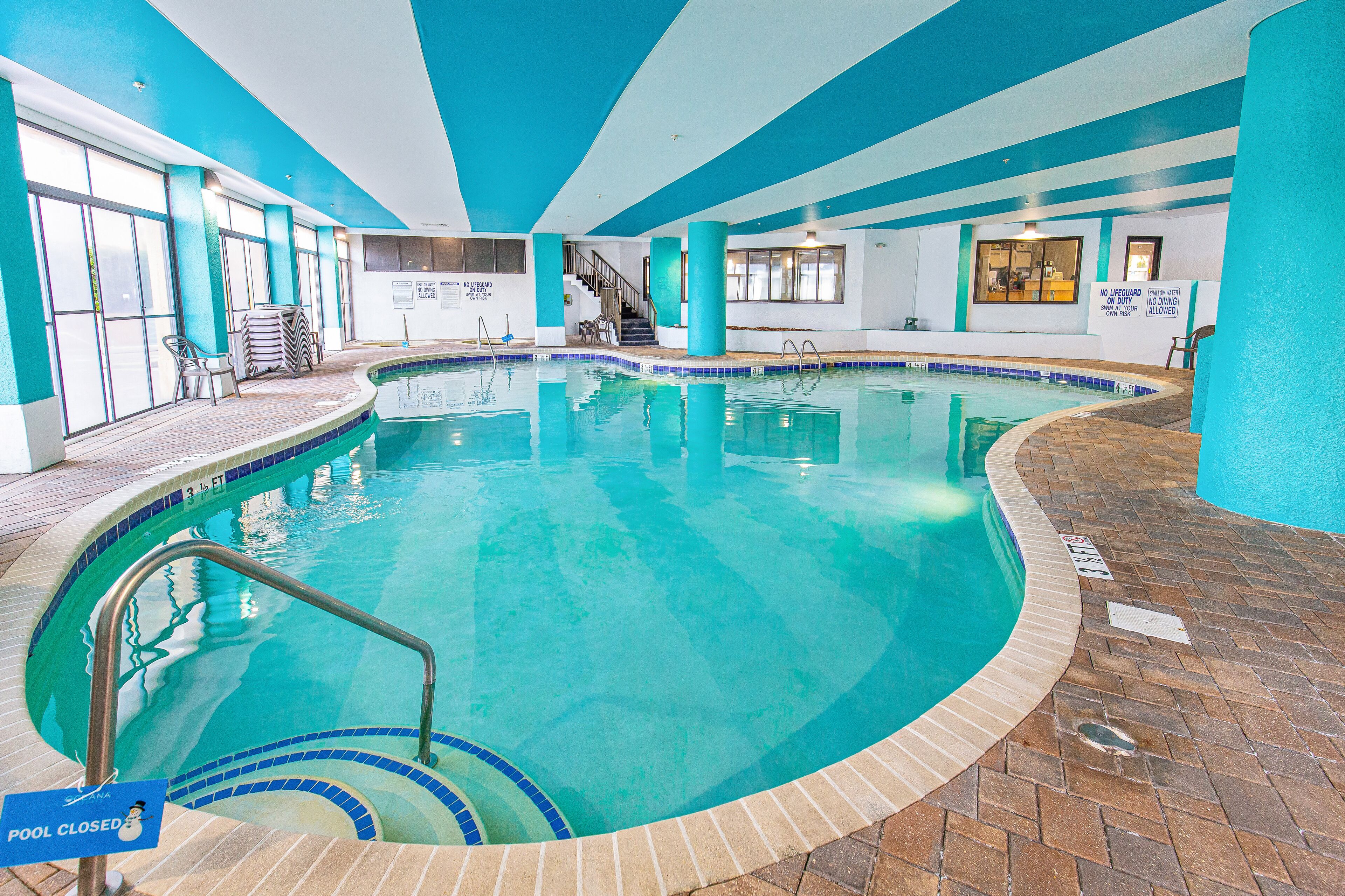 An indoor swimming pool with a closed pool sign, a staircase, and a lifeguard station.