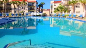 Una piscina con sillas de descanso y palmeras, rodeada de edificios de varios pisos con techos rojos.