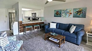 Una sala de estar moderna con un sofá azul, una mesa de centro y una cocina al fondo.