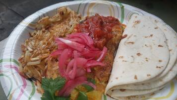 A paper plate with a meal consisting of a tortilla, a fried item, a red sauce, and pickled onions.