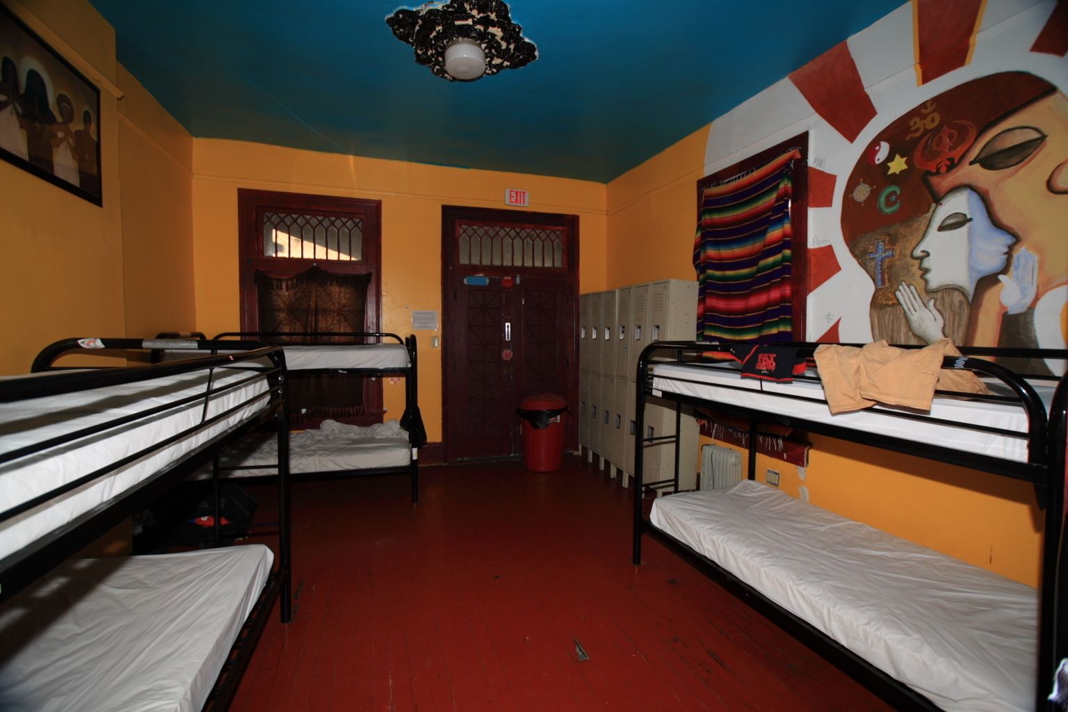 Une chambre de dortoir avec des lits superposés, des casiers et une fresque murale.