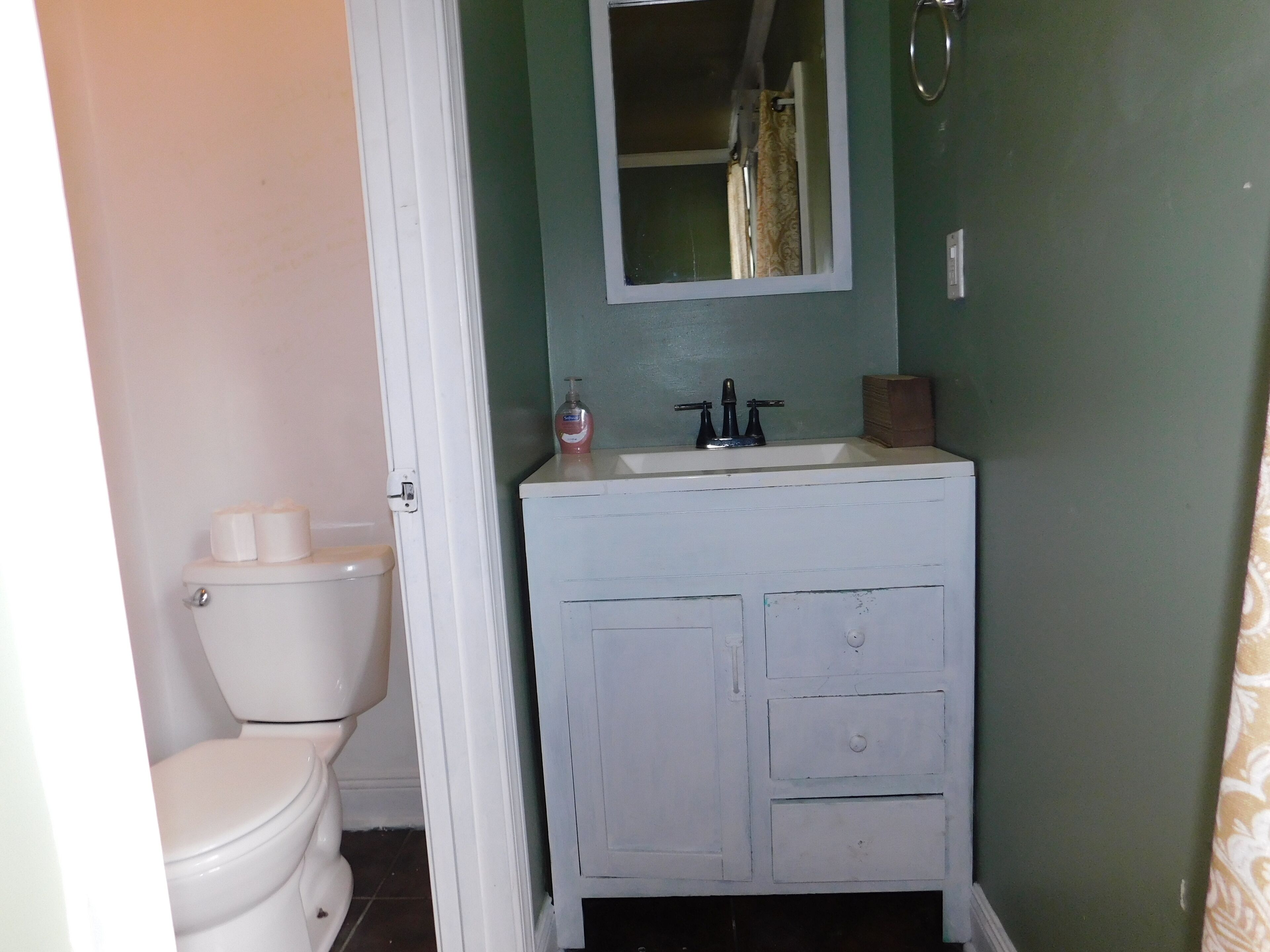 A bathroom with a white toilet, a white sink with a mirror above it, and green walls.