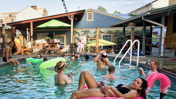 A swimming pool area with people relaxing on inflatable floats. - India House Backpackers Hostel (New Orleans)