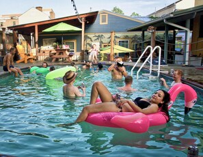 A swimming pool area with people relaxing on inflatable floats. - India House Backpackers Hostel (New Orleans)