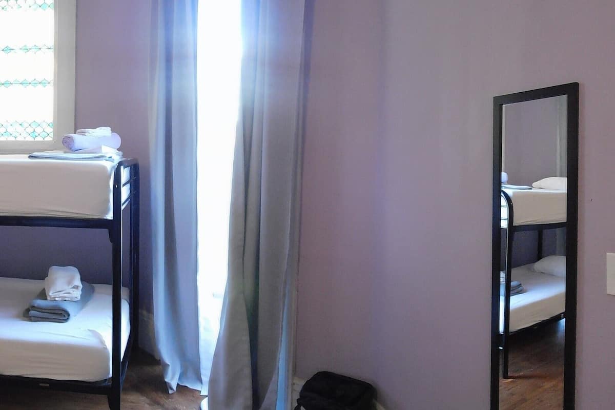 Quarto com beliche, lareira, uma janela grande com cortinas e um espelho na parede.