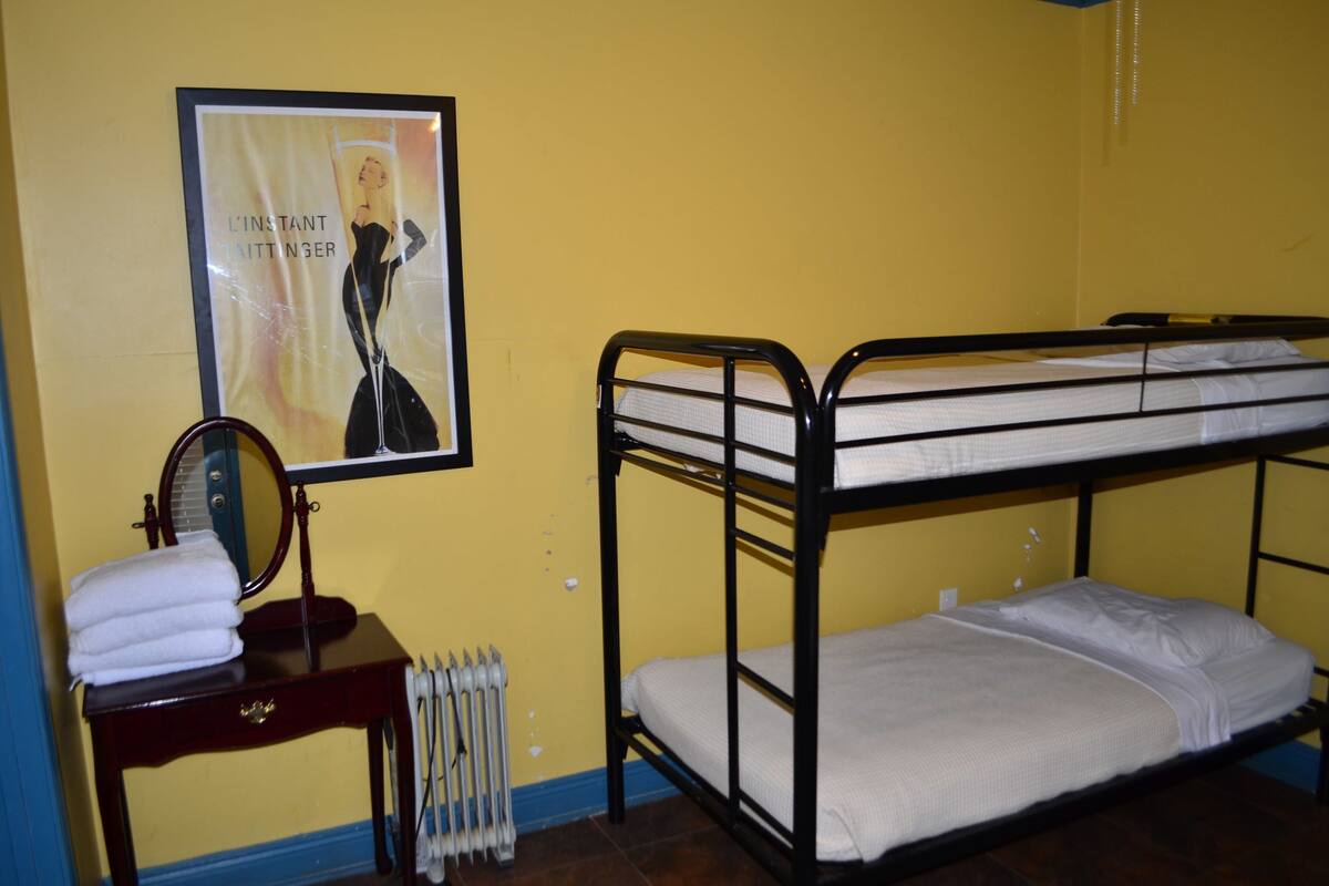 Quarto com beliche, um cartaz na parede, uma pequena mesinha de toucador com espelho e um radiador.