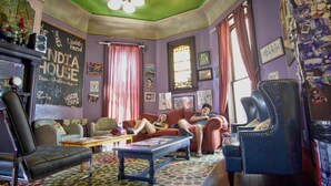 A cozy living room with a green ceiling, a red couch, a blue armchair, and a patterned rug. - India House Backpackers Hostel (New Orleans)