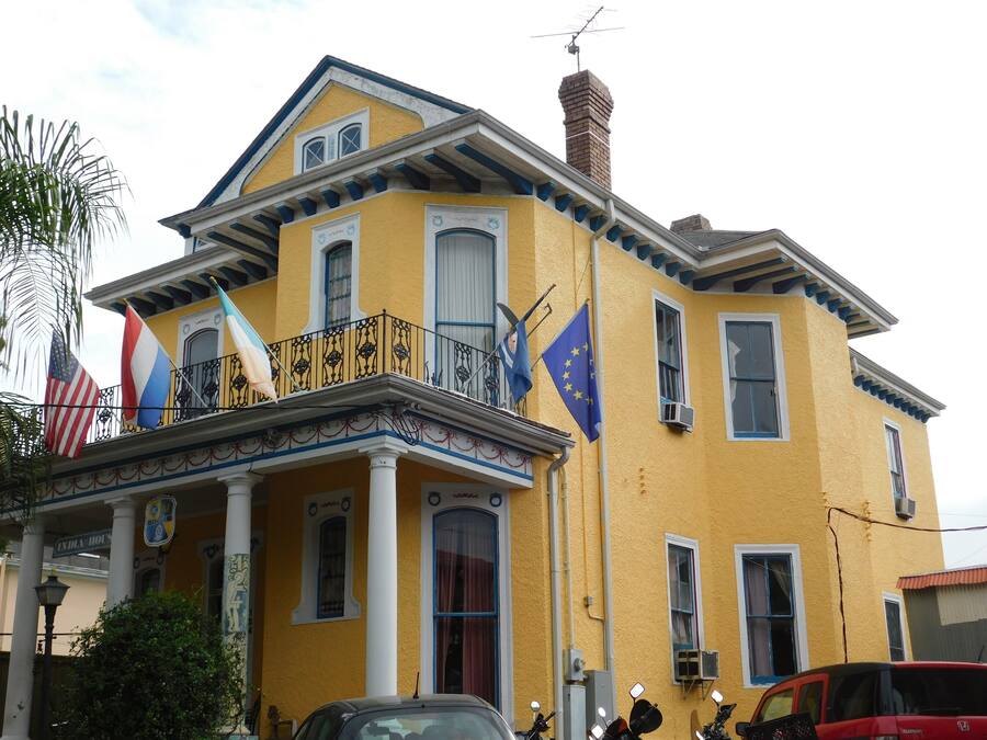 A yellow building with a balcony, multiple flags, and a chimney.