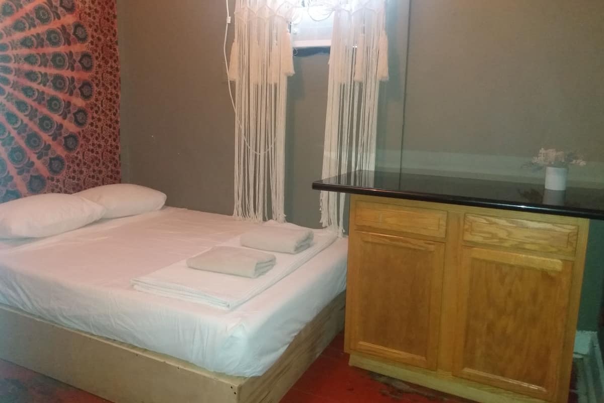 Quarto com cama, cortinas brancas, um armário de madeira e tapeçaria estampada.