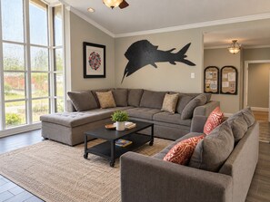 A modern living room with a sectional sofa, a coffee table, and a large fish wall art piece.