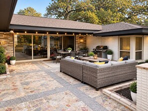 A covered patio area with a dining table and chairs, a large wicker sofa, and a barbecue grill.