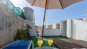 A rooftop terrace with two glasses of orange juice, a table, and a lounge chair.