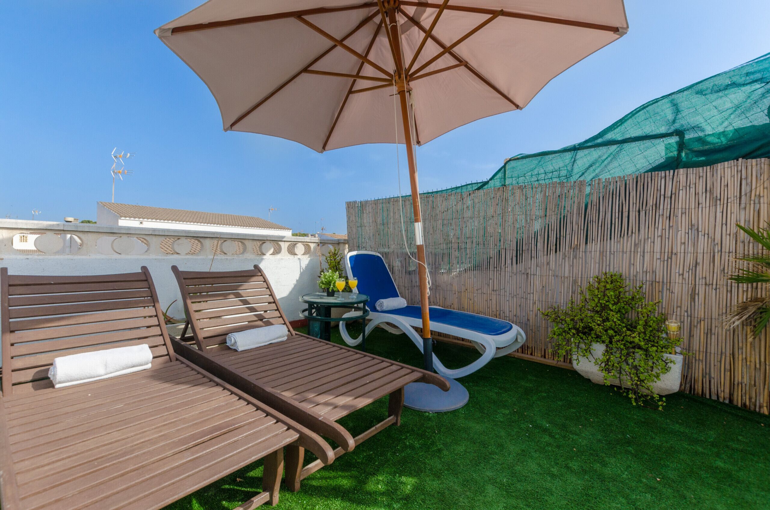 A rooftop terrace with a wooden lounge area, a blue lounge chair, and a large umbrella.