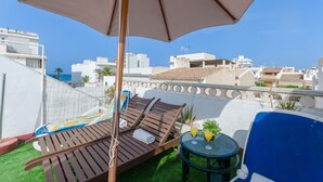 A rooftop terrace with two wooden lounge chairs, a table with drinks, and a large umbrella.