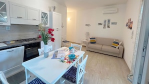 A compact living space with a kitchenette, a dining table with chairs, a sofa, and a wall-mounted air conditioner. - Apartment Ancora on the sea (Marina di Grosseto)