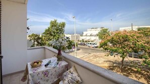 A balcony with a table, a vase with flowers, and a view of a street with cars and buildings. - Dolce Mimi - Two Bedroom House, Sleeps 4 (Pescoluse)