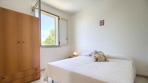 A bedroom with a bed, a wooden wardrobe, a window, and a small bedside table with a lamp. - Dolce Mimi - Two Bedroom House, Sleeps 4 (Pescoluse)