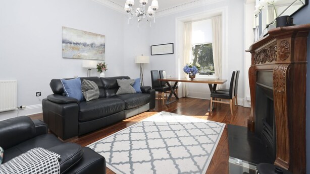 Uma sala de estar com um sofá de couro preto, uma mesa de jantar de madeira e uma lareira.