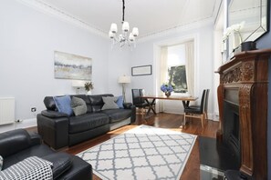 A living room with a black leather sofa, a wooden dining table, and a fireplace. - Fantastic New Town Flat with Shared Garden (Edinburgh)