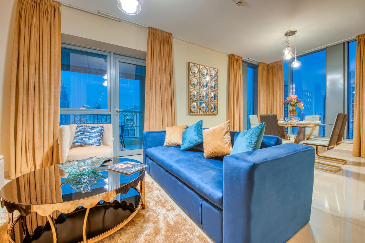 A modern living room with a blue sofa, a glass coffee table, and a city view through large windows.
