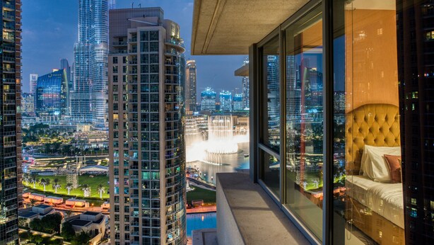 A high-rise hotel room with a city view, large windows, and a modern bed.