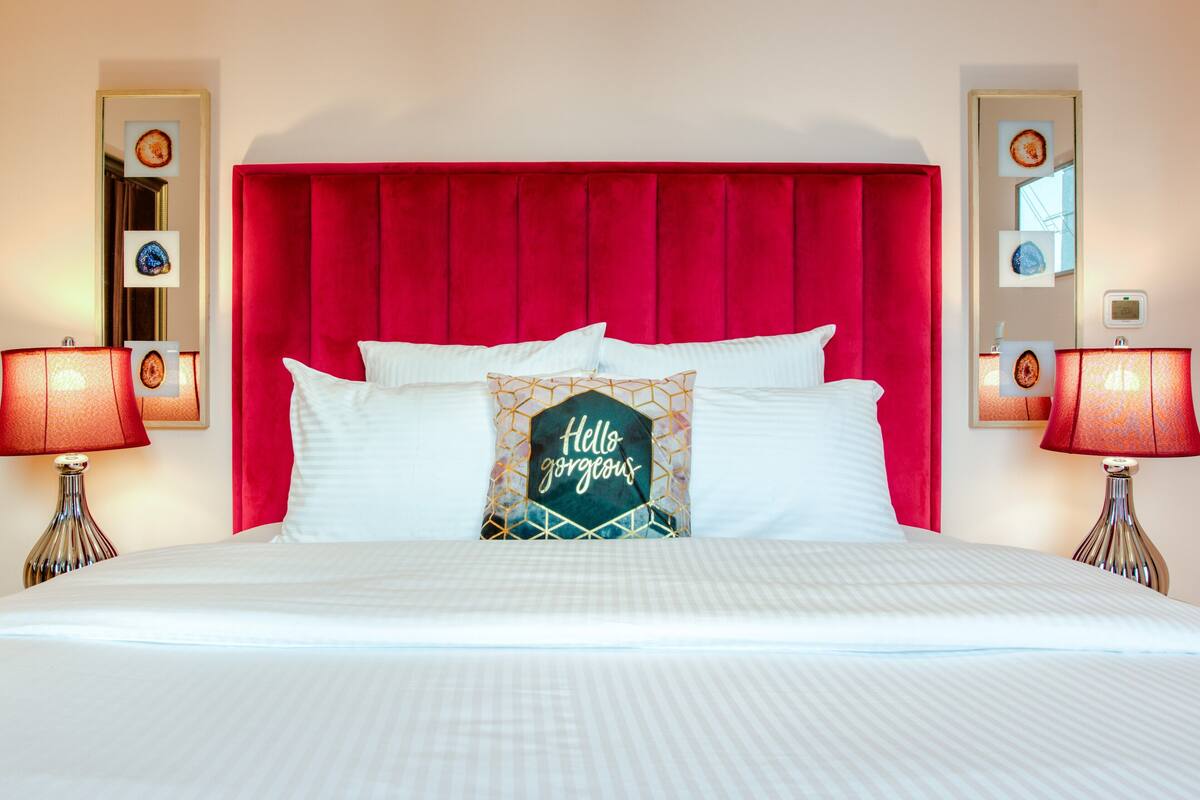 A hotel room with a red upholstered headboard, white bedding, and decorative pillows.