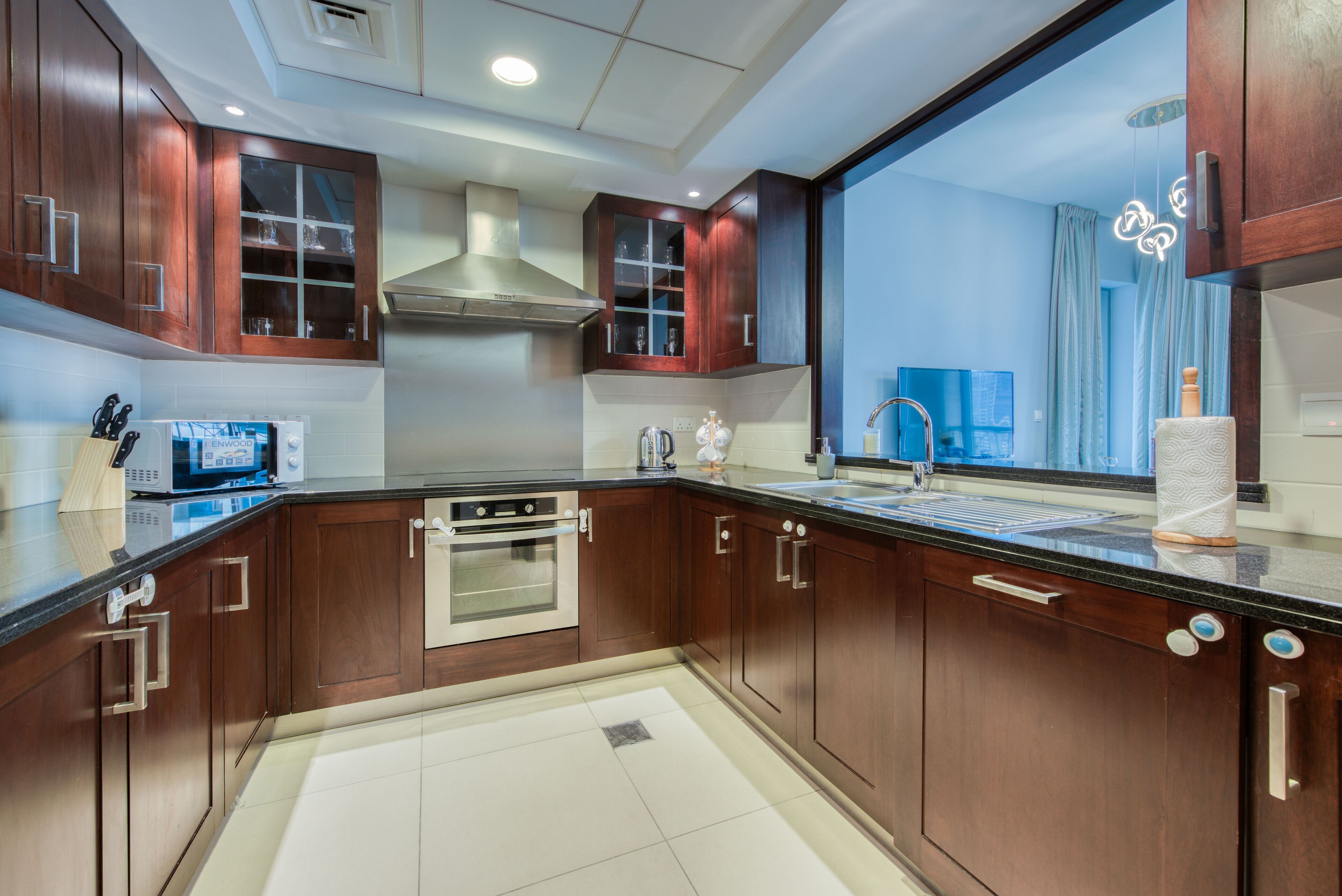 A modern kitchen with wooden cabinets, stainless steel appliances, and a large window with a view of the sky.