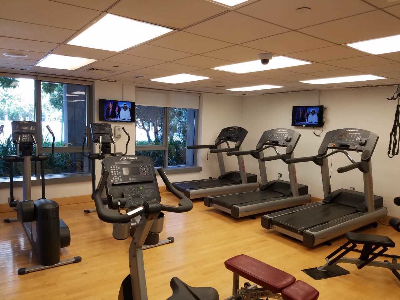 A gym with treadmills, elliptical machines, and a bench.
